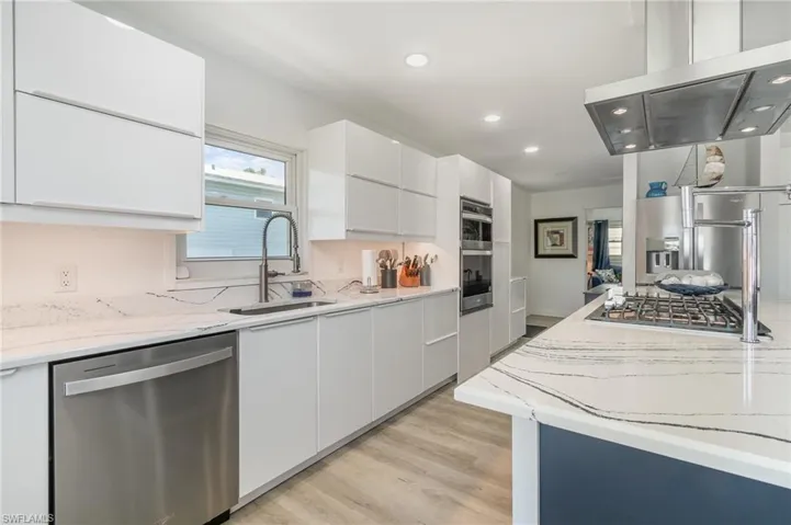 Kitchen featuring modern cabinets, stainless steel appliances, light stone countertops, ventilation hood, and white cabinets