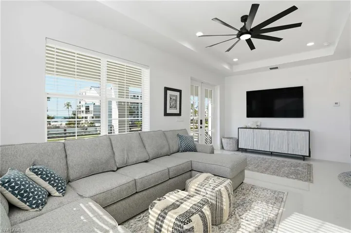 Living room with a tray ceiling, recessed lighting, a ceiling fan, and French doors e