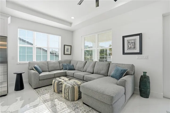 Living room featuring a raised ceiling, light marble finish flooring, a ceiling fan, and recessed lighting
