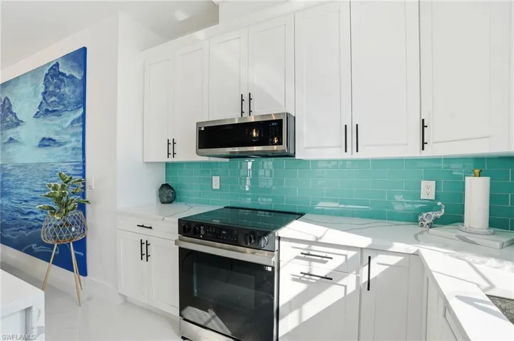 Kitchen featuring white cabinets, appliances with stainless steel finishes, light stone counters, decorative backsplash, and light marble finish flooring