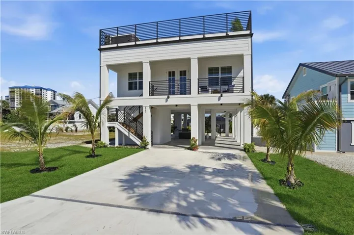 Raised beach house with a carport, concrete driveway, stairs, a front yard, and a patio
