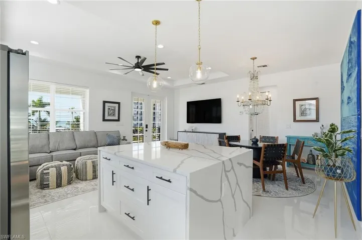 Kitchen with white cabinets, pendant lighting, stainless steel fridge, light stone countertops, and open floor plan