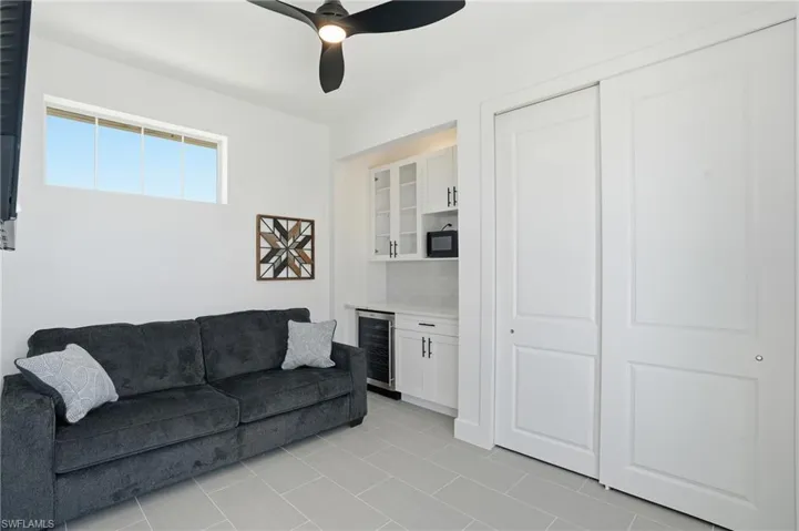 Living room featuring wine cooler, a bar, a ceiling fan, and light tile patterned flooring