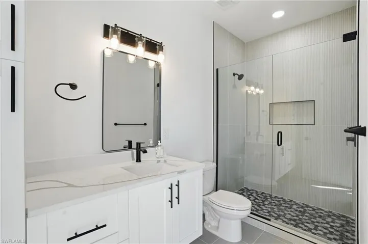 Bathroom with a shower stall, vanity, light tile patterned floors, and recessed lighting