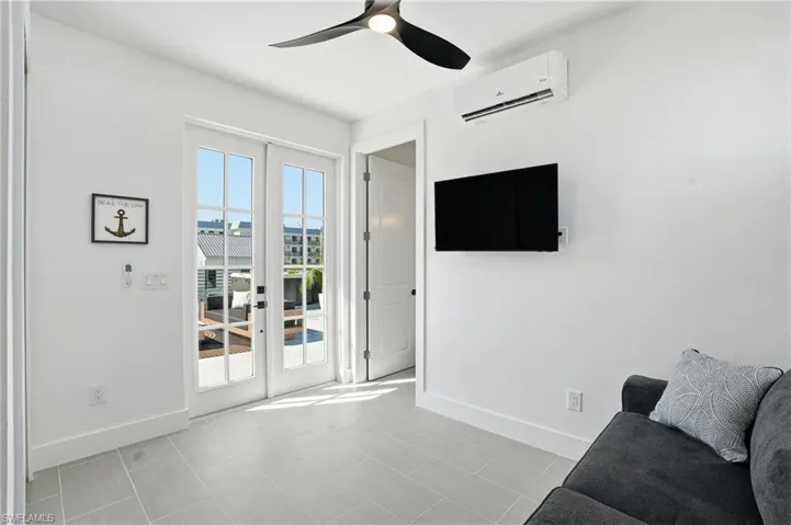 Living area featuring ceiling fan, a wall unit AC, and French doors