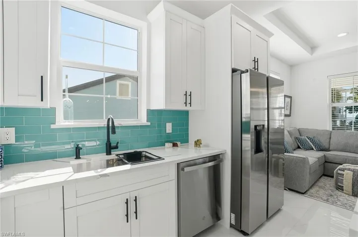 Kitchen with open floor plan, appliances with stainless steel finishes, light stone counters, and white cabinets