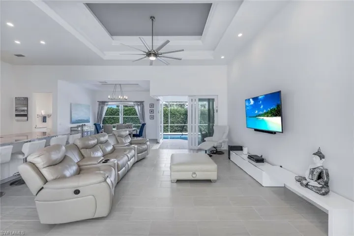 Tiled living room with ceiling fan, tray ceiling and pool views.