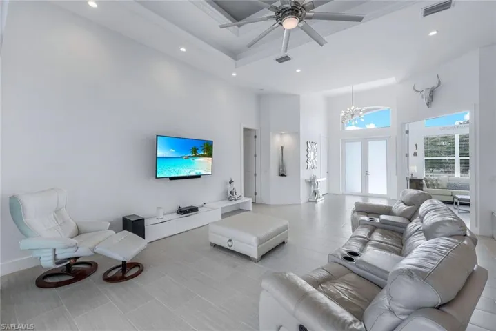 Spacious living room with a towering tray ceiling, ceiling fan, tile floors and pool views.