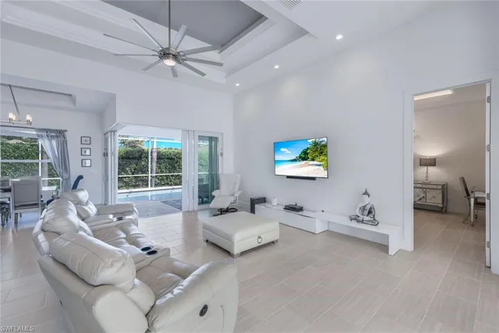 Living room with a towering tray ceiling, ceiling fan, tile floors and pool views.
