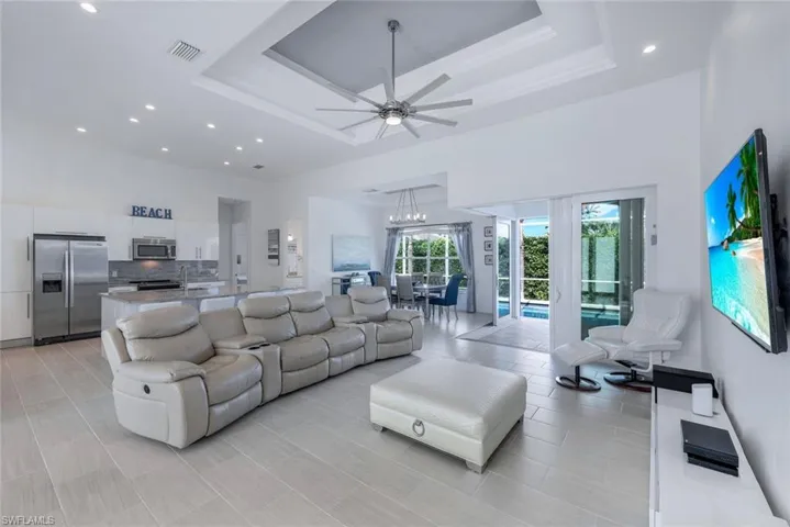Open floor plan, tiled living room with ceiling fan, tray ceiling and pool views