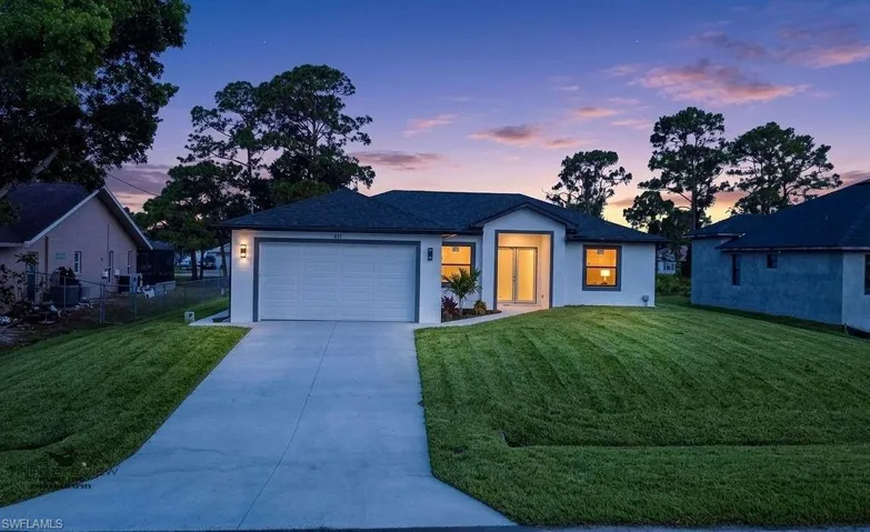 Modern stucco exterior with a dark shingle roof, integrated two-car garage, concrete driveway, and a manicured lawn