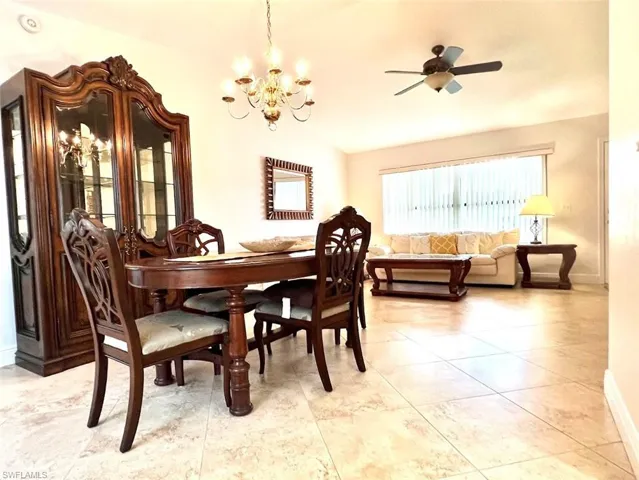 Dining room with light tile patterned floors, ceiling fan with notable chandelier, and lofted ceiling