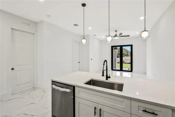Kitchen featuring dishwasher, light stone counters, light marble finish flooring, and decorative light fixtures