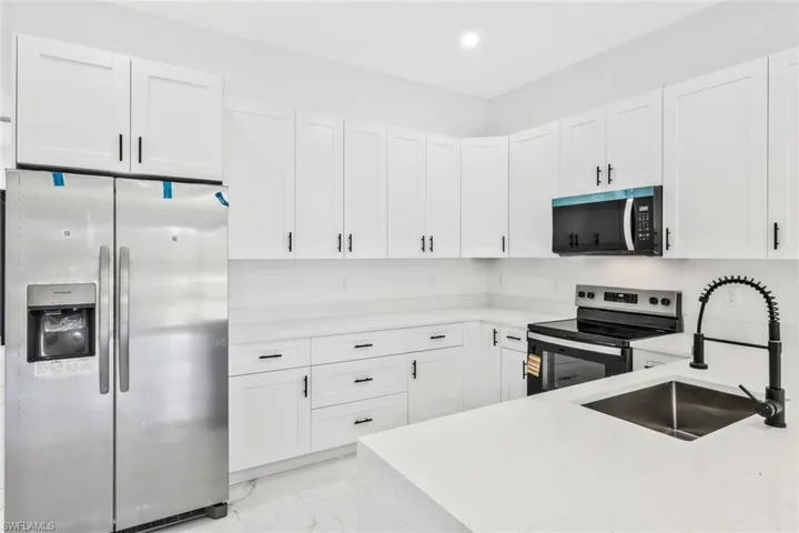 Kitchen with stainless steel appliances, white cabinetry, light stone countertops, recessed lighting, and light marble finish flooring