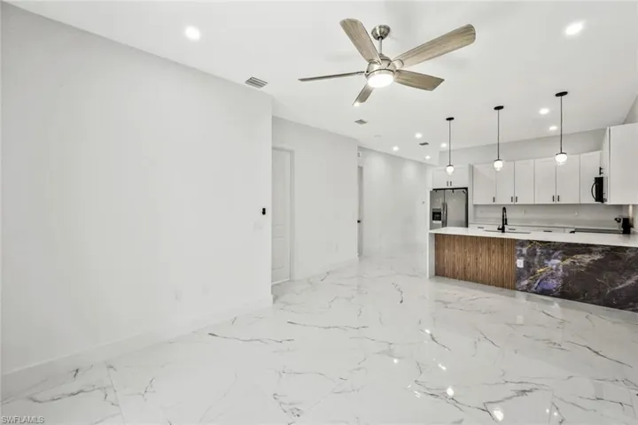 Kitchen with open floor plan, black appliances, a ceiling fan, hanging light fixtures, and light stone countertops