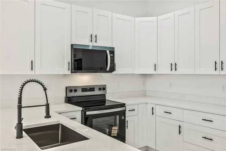 Kitchen with stainless steel appliances, white cabinets, and light stone counters