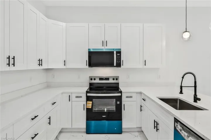 Kitchen featuring range with electric cooktop, white cabinetry, stainless steel microwave, light stone counters, and hanging light fixtures