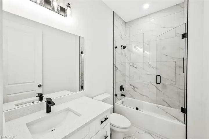 Full bath featuring vanity, combined bath / shower with glass door, marble look tile flooring, and recessed lighting