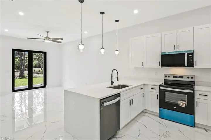 Kitchen with stainless steel appliances, a peninsula, white cabinetry, and light stone countertops