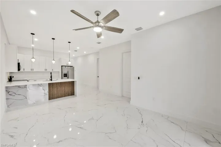 Kitchen with open floor plan, pendant lighting, stainless steel refrigerator with ice dispenser, a ceiling fan, and a kitchen island