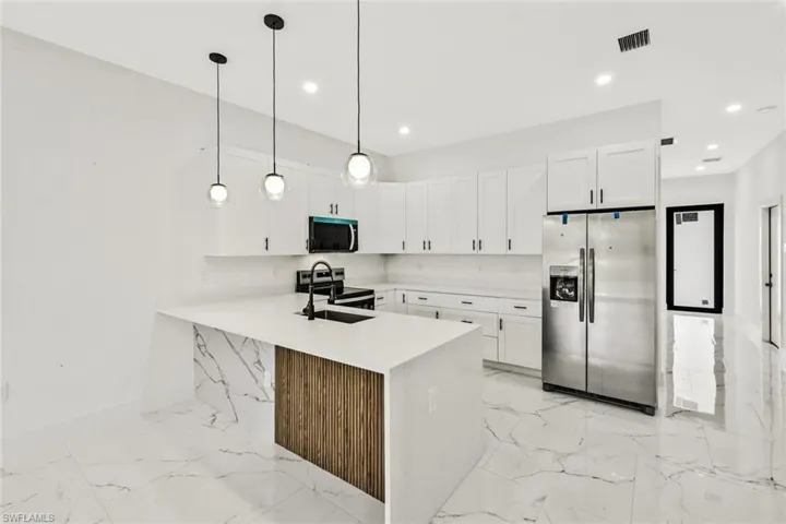 Kitchen with stainless steel appliances, light stone counters, white cabinets, a peninsula, and pendant lighting