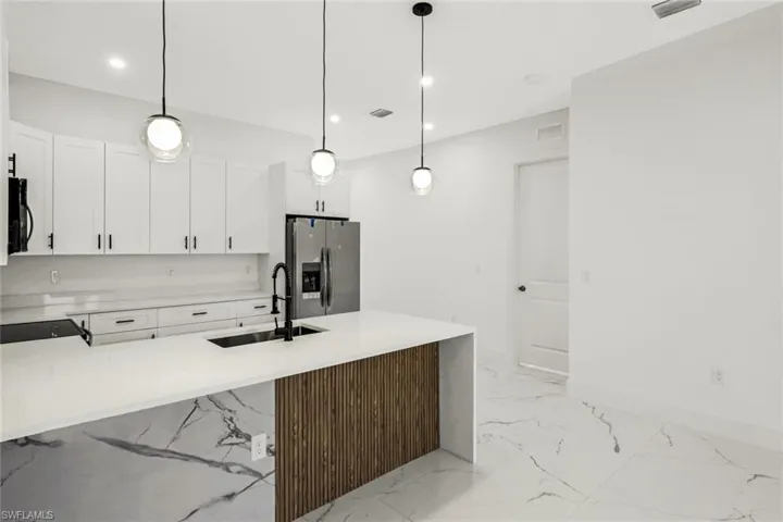 Kitchen with light stone counters, black appliances, white cabinetry, a peninsula, and hanging light fixtures