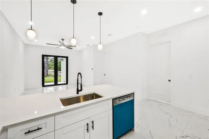 Kitchen with dishwasher, light marble finish flooring, light stone counters, white cabinetry, and decorative light fixtures