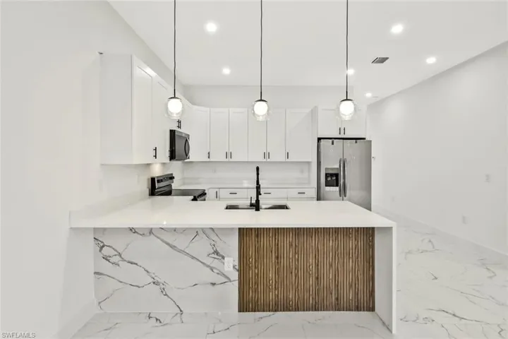 Kitchen with a peninsula, light stone counters, stainless steel appliances, and white cabinetry