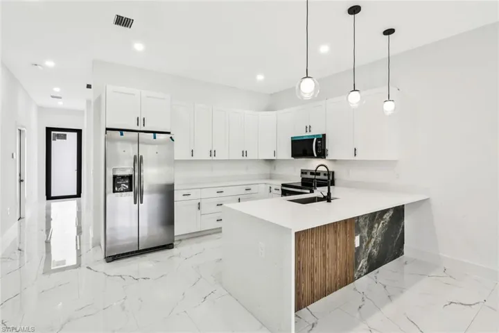 Kitchen with light stone counters, stainless steel appliances, white cabinets, hanging light fixtures, and a peninsula