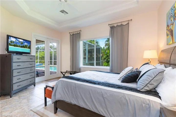 Bedroom with ceiling fan, a tray ceiling, french doors, and access to exterior