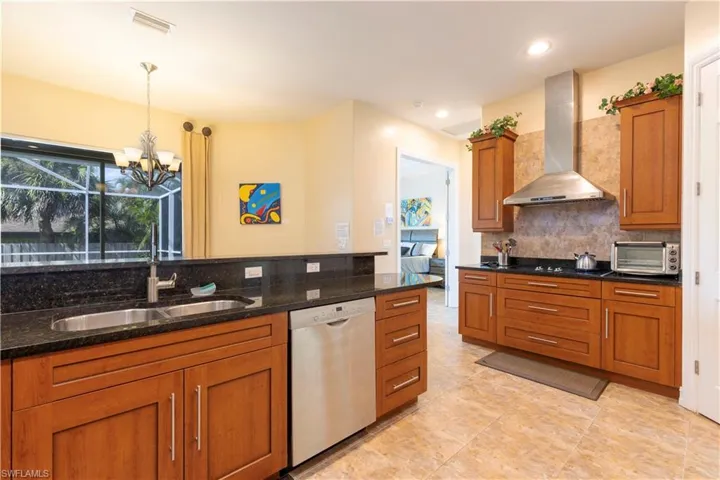 Kitchen featuring wall chimney exhaust hood, dark stone counters, decorative light fixtures, and stainless steel dishwasher