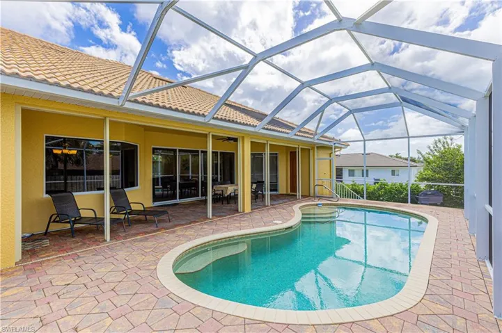 View of pool with glass enclosure, a patio area, and ceiling fan