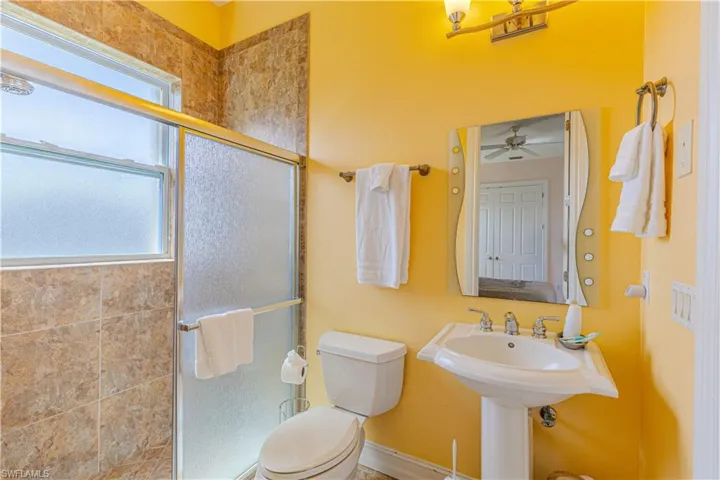 Bathroom featuring walk in shower, toilet, and ceiling fan