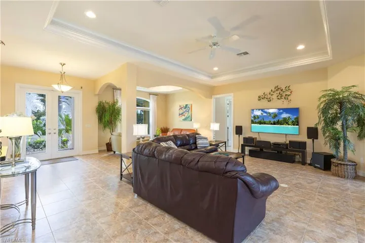 Living room with a raised ceiling, french doors, ornamental molding, and ceiling fan