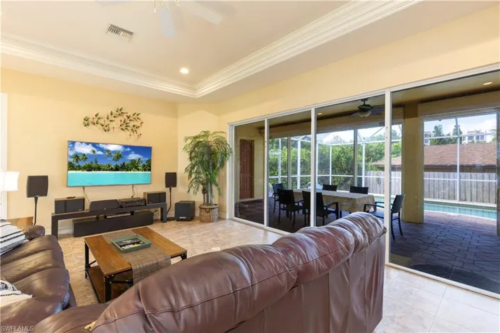 Living room featuring ceiling fan, a tray ceiling, crown molding, and light tile patterned floors