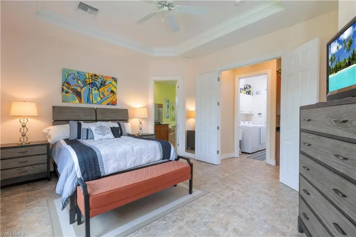 Bedroom featuring ornamental molding, a tray ceiling, connected bathroom, and ceiling fan