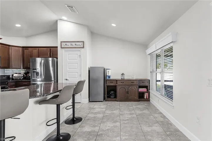 Kitchen with dark wood finish cabinets, a breakfast bar, dark stone counters, stainless steel fridge with ice dispenser, and freestanding refrigerator