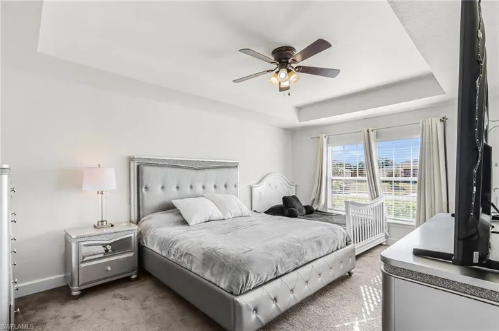 Bedroom with light colored carpet, ceiling fan, and a raised ceiling