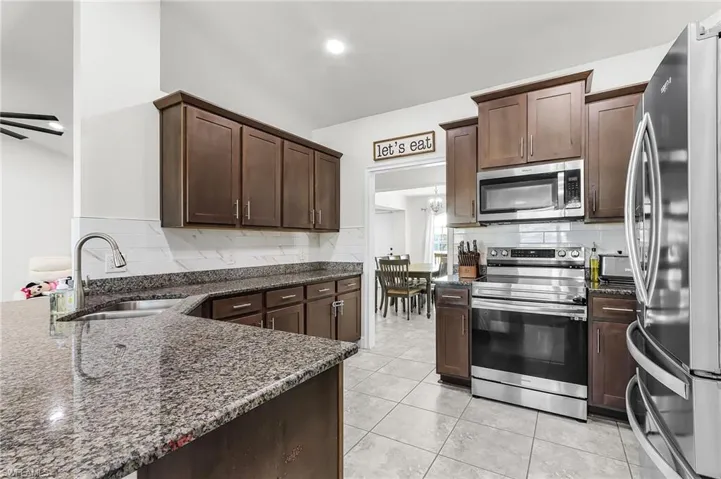 Kitchen featuring dark wood finish cabinets, stainless steel appliances, dark stone counters, and backsplash