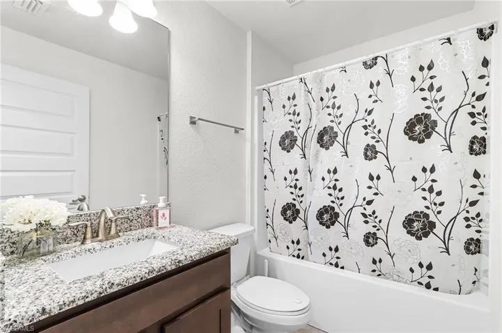 Bathroom with a textured wall, vanity, and shower / tub combo