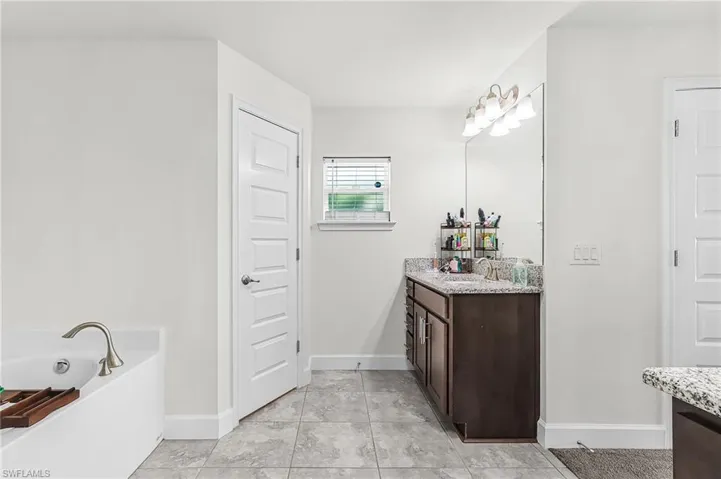 Bathroom with vanity, a garden tub, and light tile patterned flooring