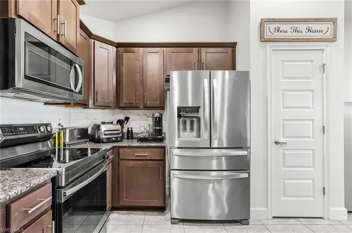Kitchen featuring stainless steel appliances, light stone countertops, light tile patterned flooring, and dark wood finish cabinetry