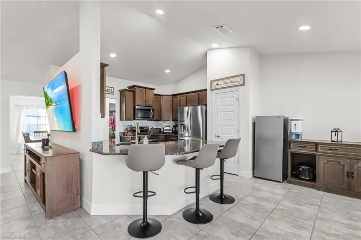Kitchen featuring dark wood finish cabinetry, dark stone countertops, a breakfast bar area, stainless steel appliances, and vaulted ceiling