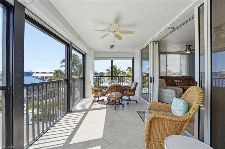 Sunroom / solarium featuring ceiling fan, a textured ceiling, a balcony, and tile patterned flooring - Virtually Edited Image
