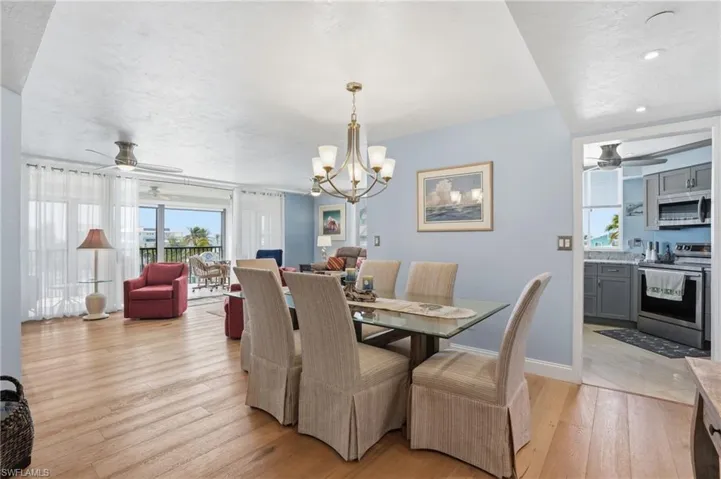 Dining area with ceiling fan, light wood-style floors, and a chandelier - Virtually Edited Image