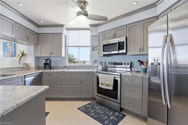 Kitchen with gray cabinetry, stainless steel appliances, light stone counters, ornamental molding, and ceiling fan - Virtually Edited Image