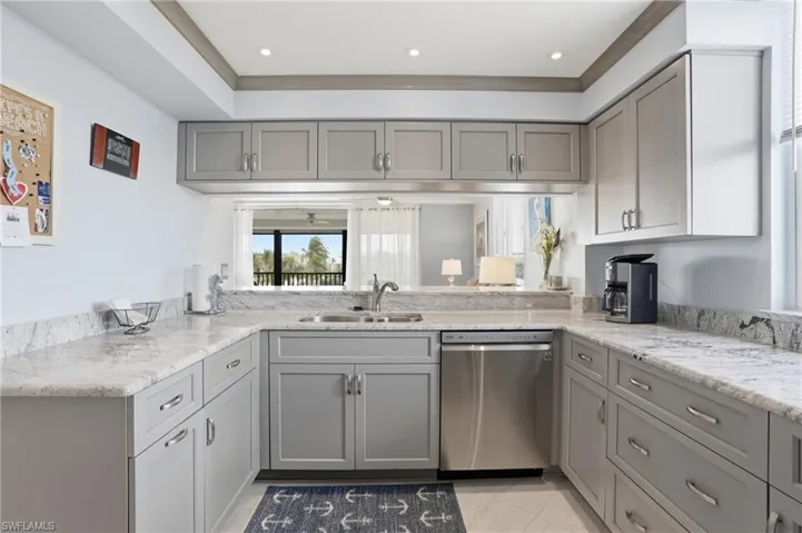 Kitchen featuring gray cabinetry, stainless steel dishwasher, light stone counters, recessed lighting, and light tile patterned flooring - Virtually Edited Image