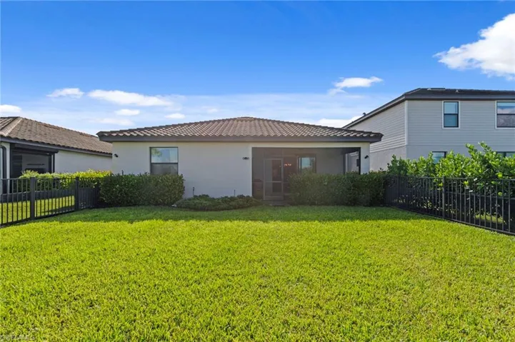 Expansive green lawn with mature perimeter landscaping and black fencing