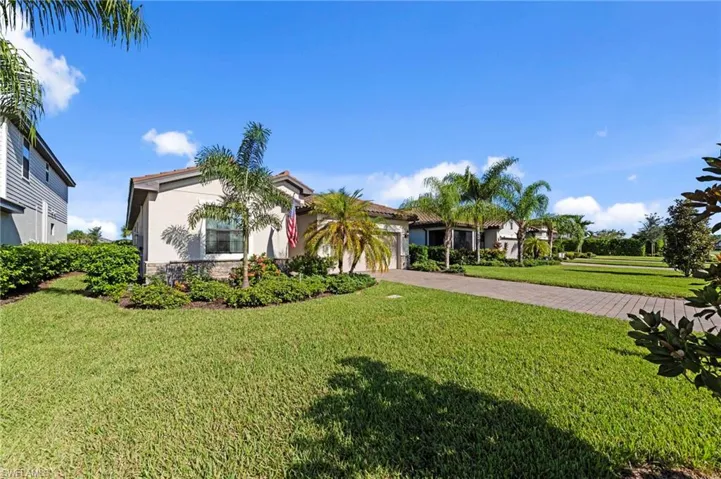 Stucco exterior with stone veneer accents, tile roof, lush landscaping featuring palm trees, and a paver driveway