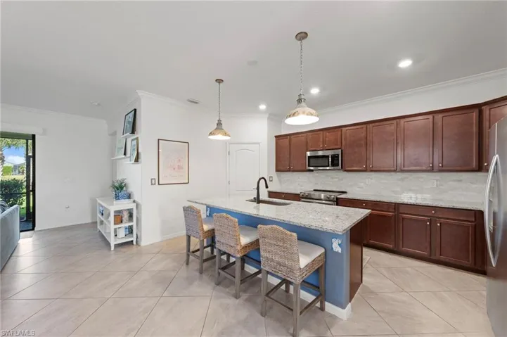 Expansive kitchen featuring a large island with seating, stainless steel appliances, abundant cabinetry, and light-toned tile flooring